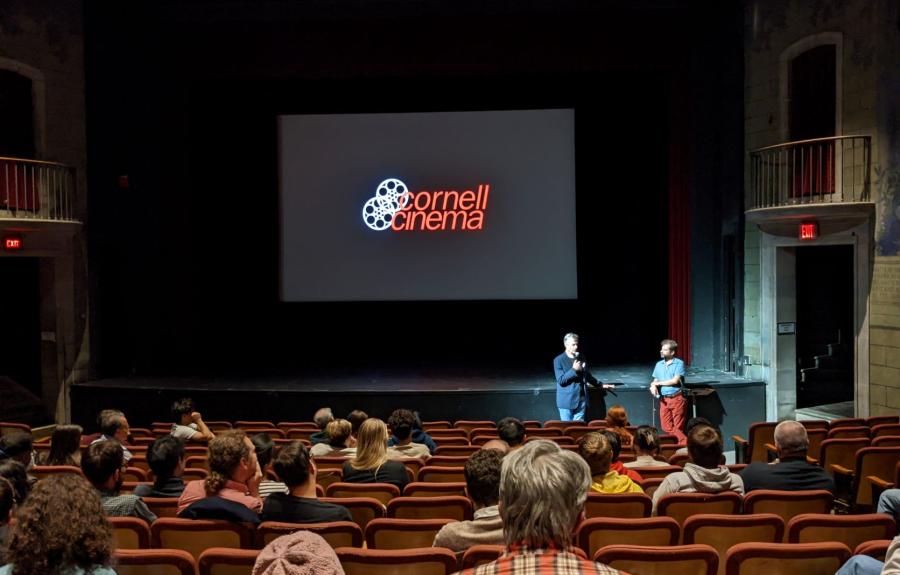 Two men standing before audience with Cornell Cinema logo behind them.