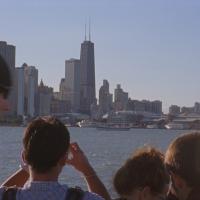 A group of people taking photos of a city skyline from a boat.