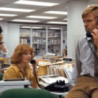 An office scene from a past era with three individuals working amidst typewriters and telephones. Desks are cluttered with papers and office equipment, suggesting a busy work environment.