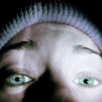 A close-up of a person’s face, focusing on the eyes which are wide open. The person is wearing a knitted hat and the lighting highlights the eyes and forehead while casting shadows over the rest of the face.