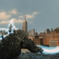 A large, dark, reptilian creature resembling Godzilla standing in a body of water with a city skyline in the background. The creature is emitting a blue beam from its mouth towards the right side of the image. The skyline features several high-rise buildi