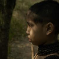 A close up of a young child looking into the distance while wearing a black beaded necklace with sunlight dabbling their face.