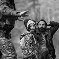 A fearful looking man and child held under arrest by a solider in camouflage fatigues.