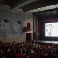 A crowded historic movie theater with an obscure black and white image on screen.