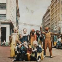 A vintage photograph of a group of people wearing carnivalesque costumes and masks while standing in the middle of an urban street.