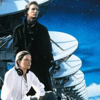 A man and a women standing in front of a row of massive white satellite dishes.