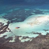 An aerial image of a boat in the ocean at the coast of an island.