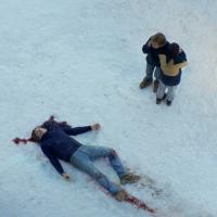 Two people standing next to a dead body in the snow with a bloody head injury.