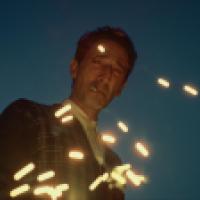 A man smoking a cigarette with sparks flying in front of his windswept face.