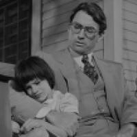 Two people sitting on a porch swing; the adult is wearing a suit and vest, while the child leans against them in a light-colored shirt, with a house in the background.