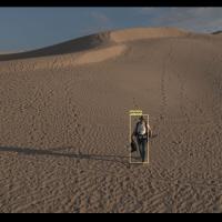 Photo of a man walking in sand dunes with a computer generated box drawn around him.