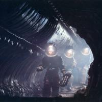 Three figures in space suits walking through a shadowy tunnel