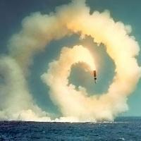 A spiral of smoke produced by a firey rocket above a large body of water.