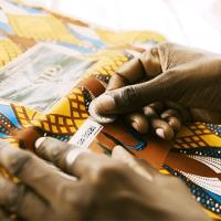 A close up image of hands weaving a colorful yellow, brown, white, and blue geometric fabric.