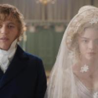 Two people in historical attire stand side by side indoors; one wears a dark blue coat with a white cravat, the other a white wedding dress with a lace veil