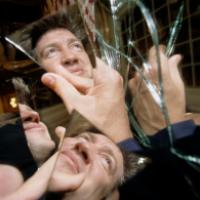A person holds a broken mirror, with reflections of their face and hands visible in the shards