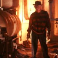 A man with a distorted face wearing a hat and gloved hand with knives attached, stands in front of an industrial background