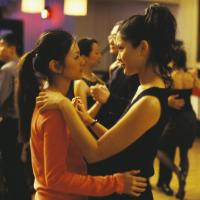 Two women dancing closely at a social event, with other dancers in the background