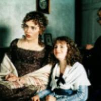 Three people in period clothing sit on a couch in a vintage setting with framed pictures and a door in the background