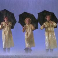 Three individuals in yellow raincoats stand in the rain holding black umbrellas; raindrops fall against a blue sky