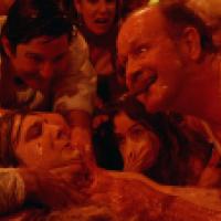 A group of people covered in a clear slime surround a person with their hands around the person's neck