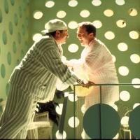 Two men wearing pastel striped pajamas laugh together in a room with polka dot walls.
