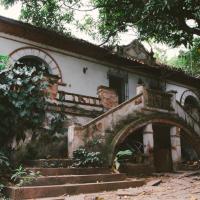 A dramatic photo of an seemingly abandoned two-story Spanish-style manor being overtaken by vines and trees.