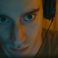 A close up image of a man wearing headphones and staring ahead intensively with a vacant expression.