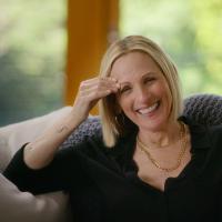 A woman with short blonde hair is laughing with one had touching her forehead.
