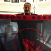 A person holds up a black cloth with red border featuring paw prints, skulls, and a stylized animal head.