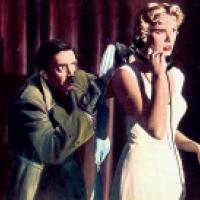 A woman in a white dress holds a black rotary phone to her ear as a man in a green coat reaches toward her with a cloth. The dark red curtains and dramatic lighting heighten the suspense of the moment.