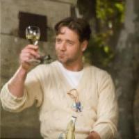 A man in a cable-knit sweater holds up a glass of white wine outdoors near a stone structure.