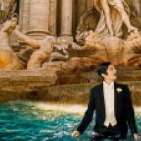 A person in a black tuxedo with a boutonnière stands waist-deep in Rome’s Trevi Fountain, gazing upward. The illuminated Baroque sculptures and cascading water behind them create a dramatic contrast with the formal attire.