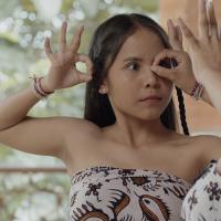 A woman with long hair and braids is dancing with her hands near her face. Her movements are being mirrored by another woman.