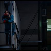 A young woman standing on a fire escape at night smoking a cigarette.