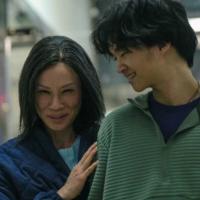 A smiling woman gently embraces a teenage boy as she walks alongside him
