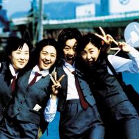 A joyful group of five girls posing in the school uniforms, which are charcoal gray with a white blouse and marron ties.