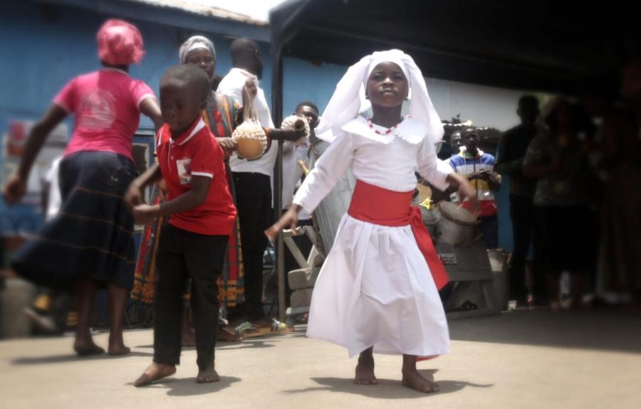 Young girl in white dress with red sash dances with young boy in red shirt
