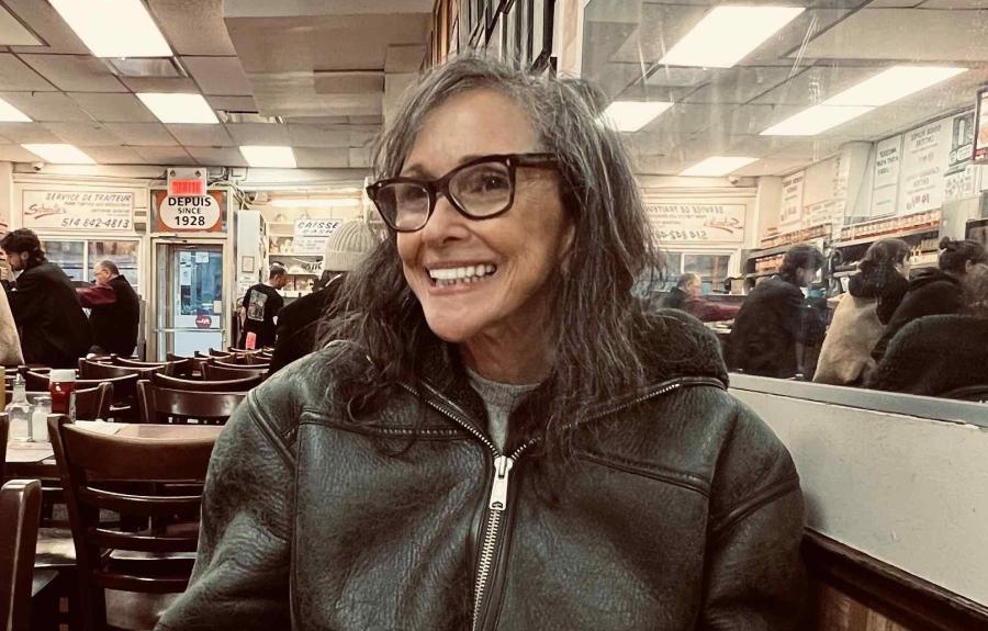 A smiling woman with glasses sitting at a table in a diner.