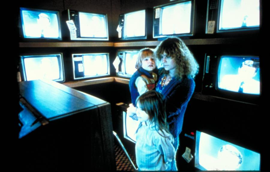 A woman and two children standing in a room filled with television screens.