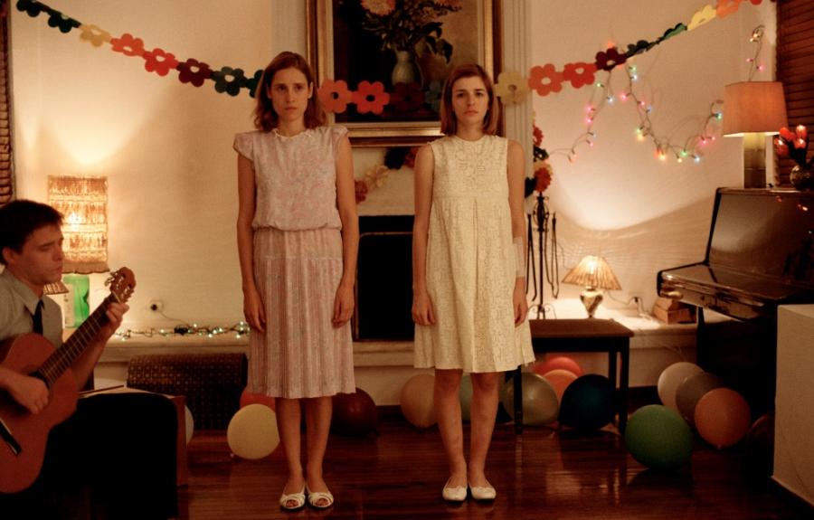 Two girls in dresses singing in a living room decorated for a party.