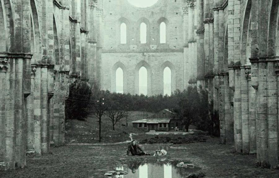 A black and white image of a man lying in the foggy ruins of a massive cathedral.