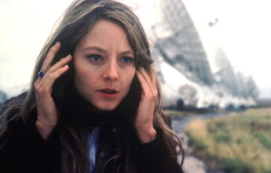 A close-up of a woman listening to headphones near massive satellites.