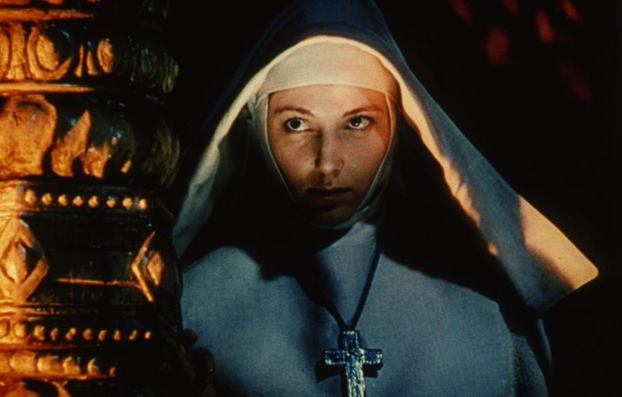 A nun wearing a habit and a cross with her face illuminated by a fire.