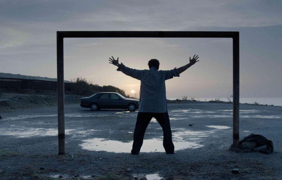 A man with arms outstretch standing in a square frame in an empty parkin lot next to the sea at dawn.