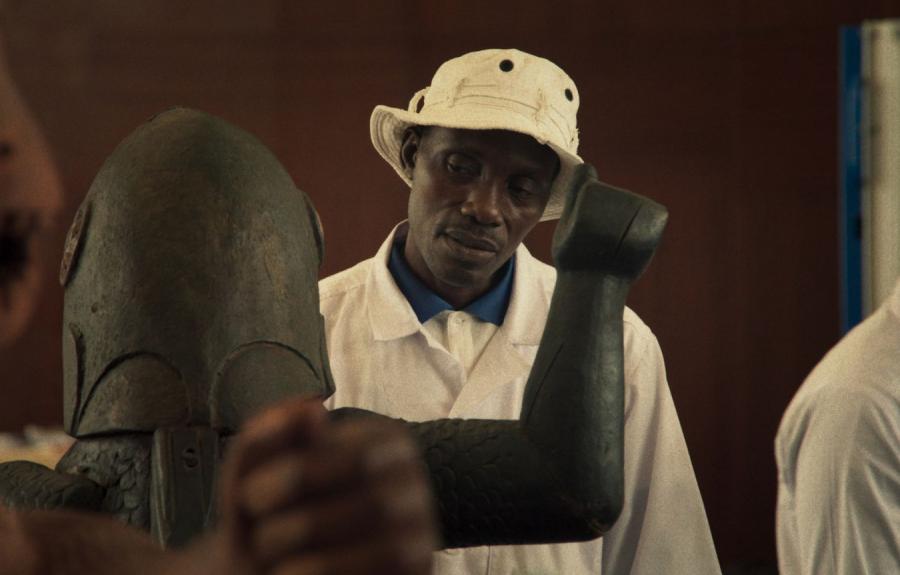 A man wearing a bucket hat and observing a statue of a warrior with its arm raised.