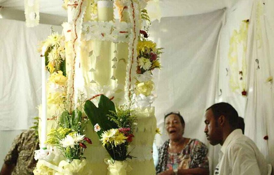 A floral and candle-decorated structure surrounded by seated individuals, set against white drapes and more floral arrangements