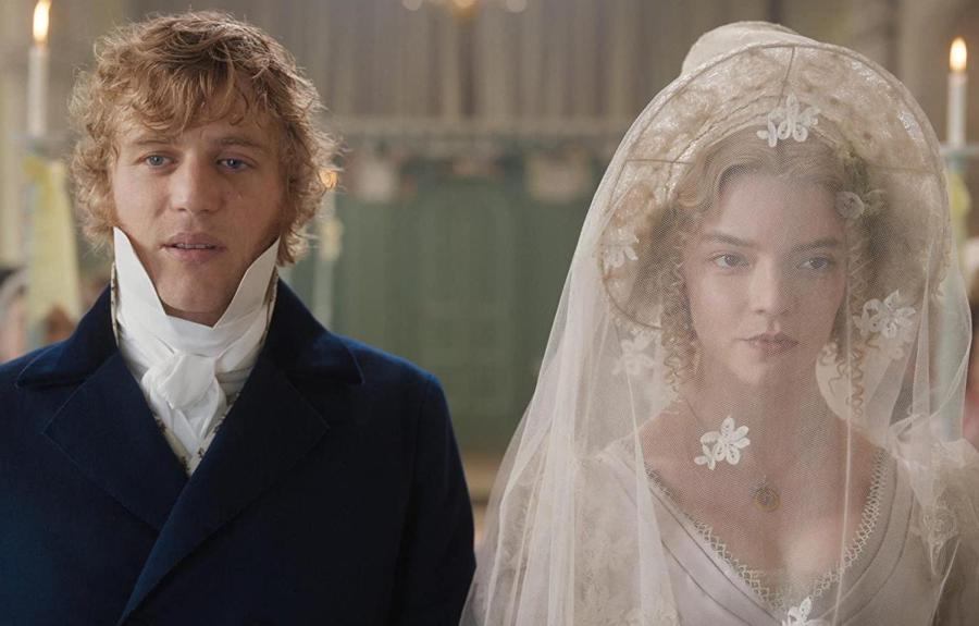 Two people in historical attire stand side by side indoors; one wears a dark blue coat with a white cravat, the other a white wedding dress with a lace veil