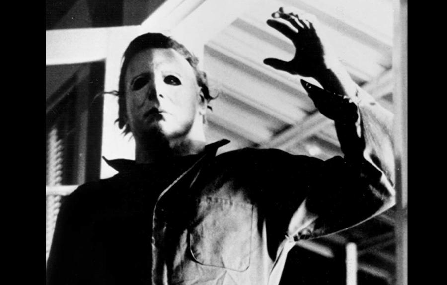 A black and white photo of a masked man with his arm raised.