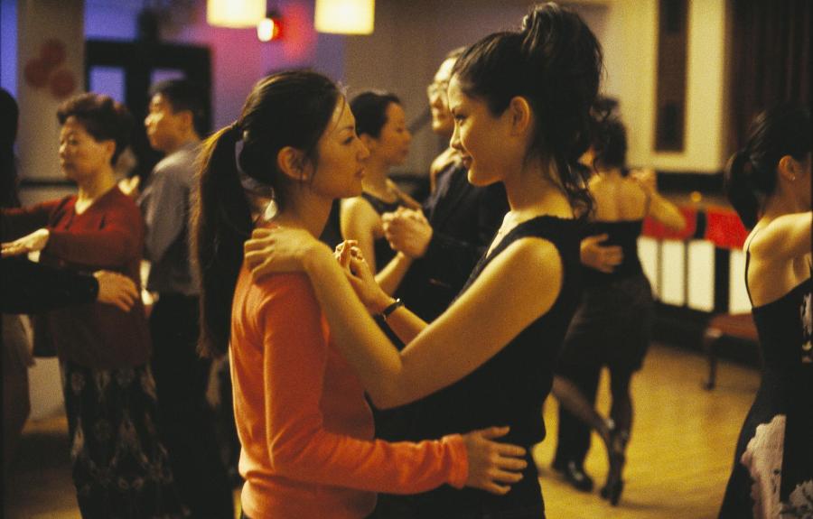Two women dancing closely at a social event, with other dancers in the background